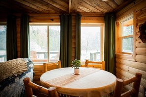 A cozy cabin interior with a round wooden table, chairs, and a window with curtains.