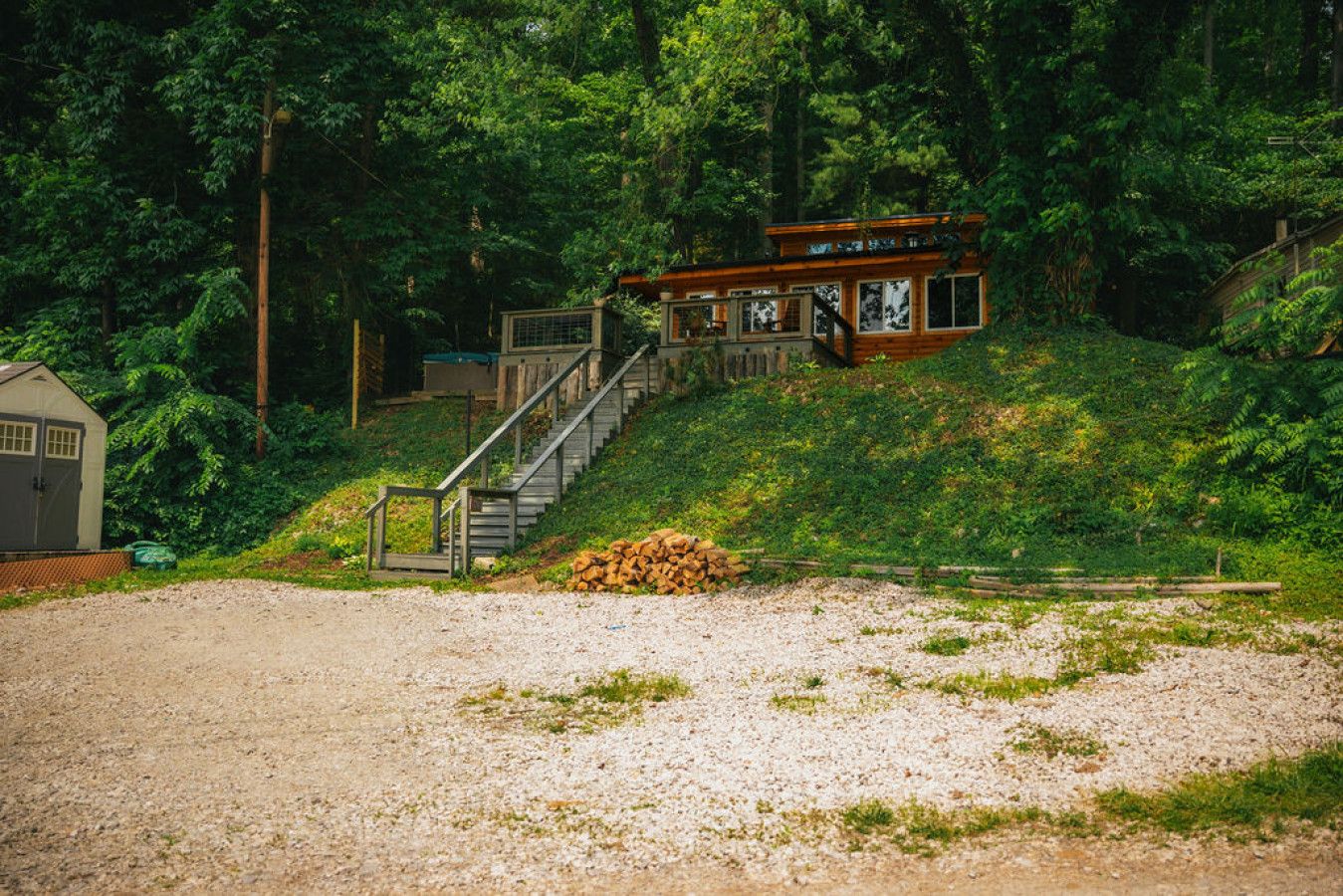 A cabin with a staircase leading to a deck, surrounded by dense forest.