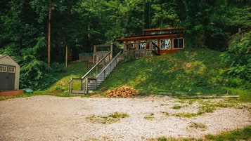 A cabin with a staircase leading to a deck, surrounded by dense forest.