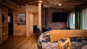 Een blokhutinterieur met een houten vloer, een bed met een gestreepte deken, een bevestigde televisie en een open haard.