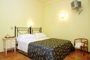Un dormitorio con cama, mesita de noche, lámpara y televisor montado en la pared.