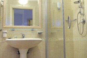 Un baño con lavamanos pedestal, cabina de ducha de cristal y espejo con marco decorativo.