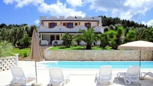 Une maison à deux étages avec une piscine et des chaises longues.