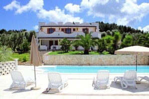 Ein zweistöckiges Haus mit Swimmingpool und Liegestühlen.
