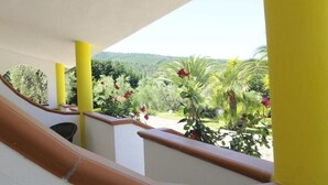 Een balkon met gele zuilen en uitzicht op een tuin met diverse planten en bloemen.