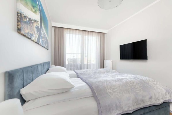 Una habitación de hotel con cama, televisión y ventana con cortinas.