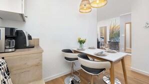 Una cocina moderna con una cafetera, dos taburetes de bar, una mesa de comedor para dos personas y una lámpara colgante.