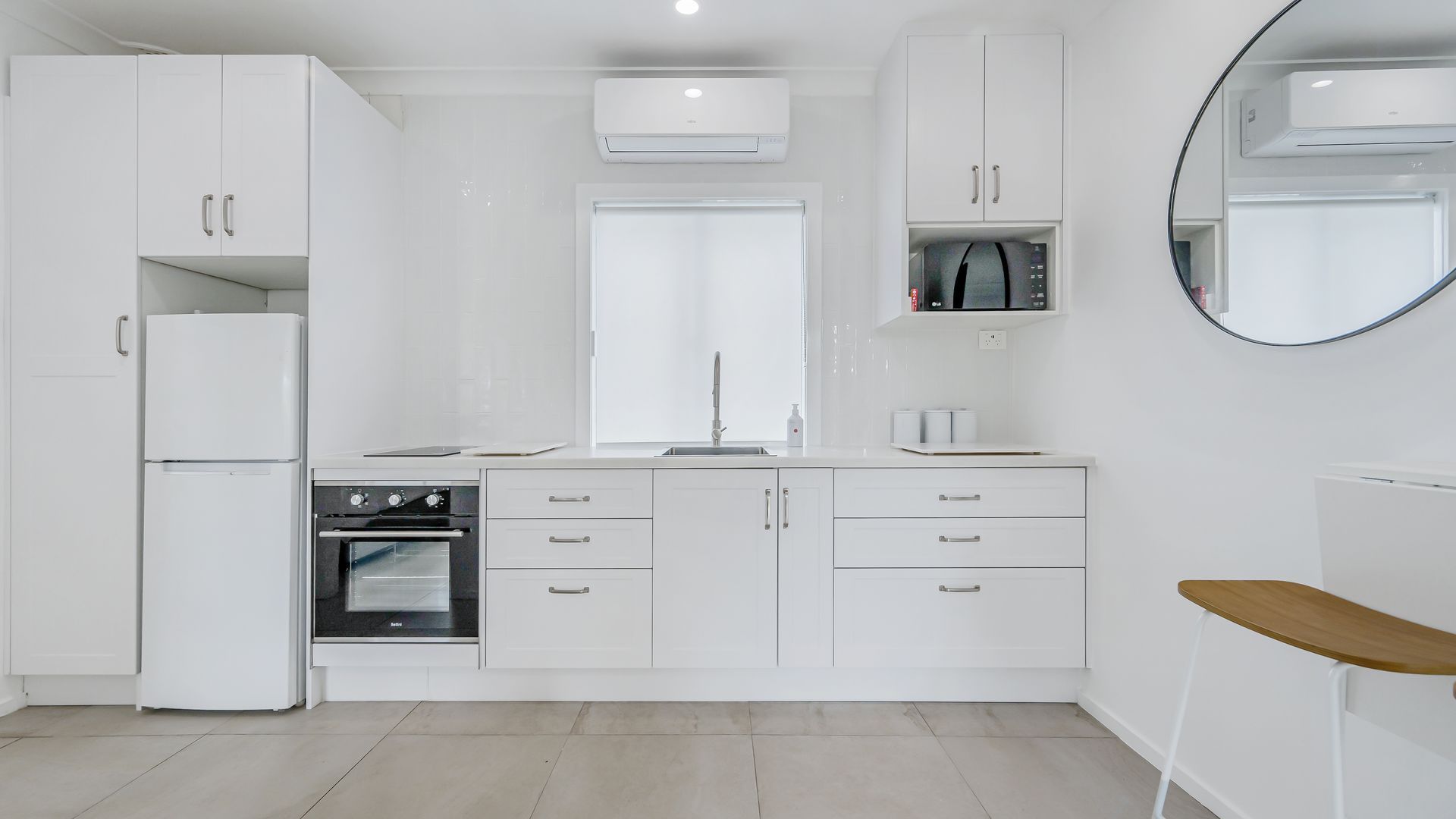 A modern kitchen with white cabinetry, a built-in oven, a microwave, and a sink.