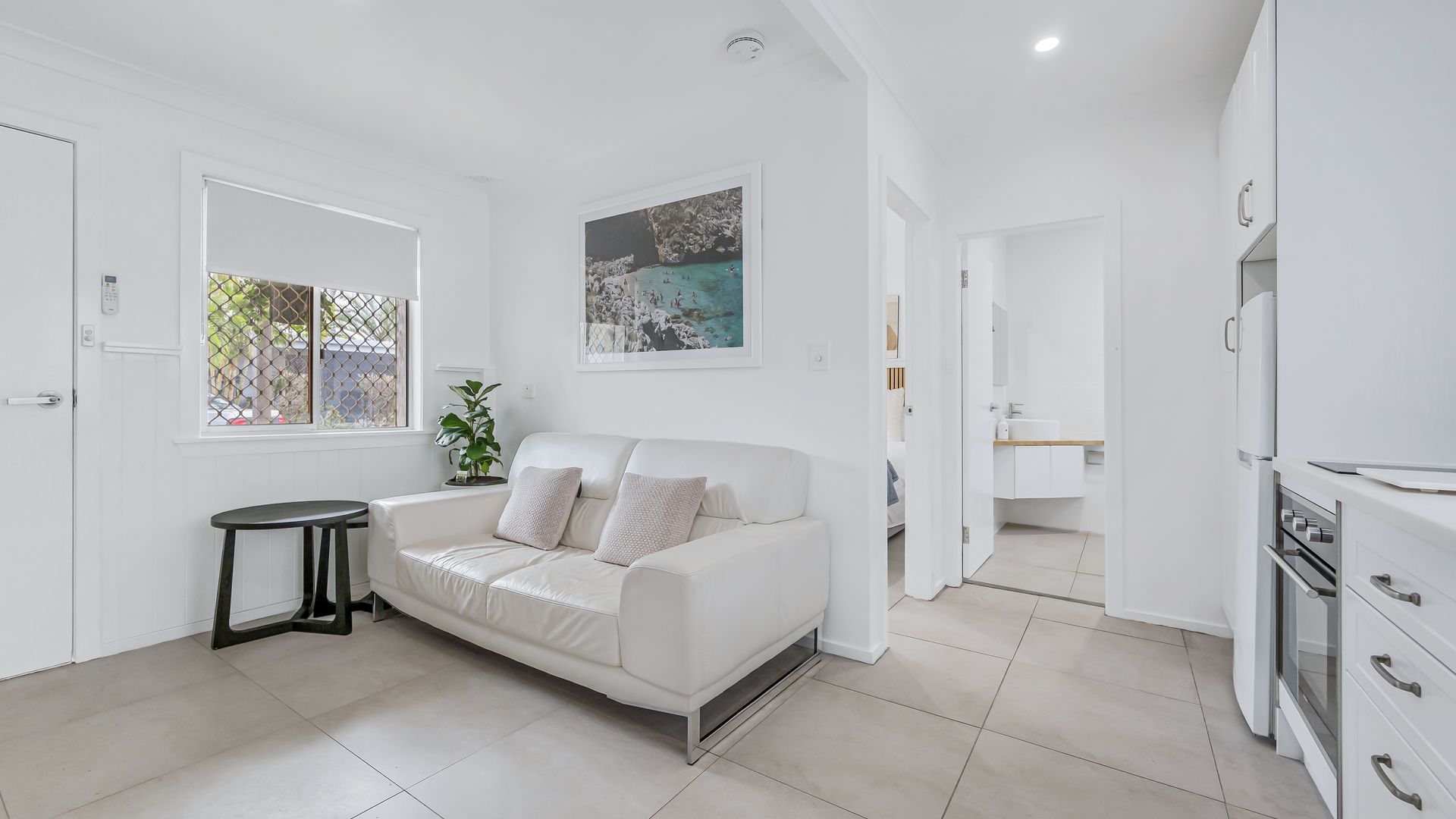 A modern, white interior with a sofa, a small table, and a kitchen area.