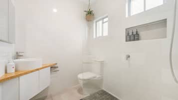 A modern bathroom with a white sink, toilet, and shower. There is a wooden countertop and a hanging plant.