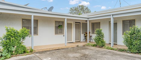 Ein zweistöckiges Wohnhaus mit überdachter Terrasse, Satellitenschüsseln und einem kleinen Garten.
