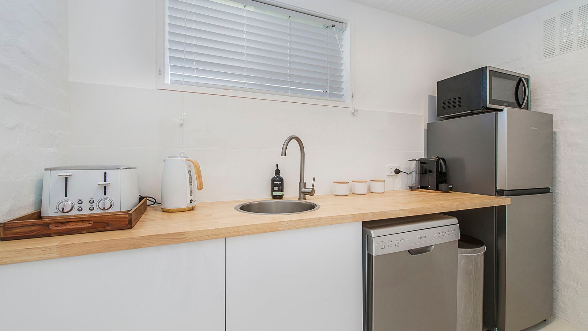 A compact kitchen with a toaster, kettle, sink, and a refrigerator.