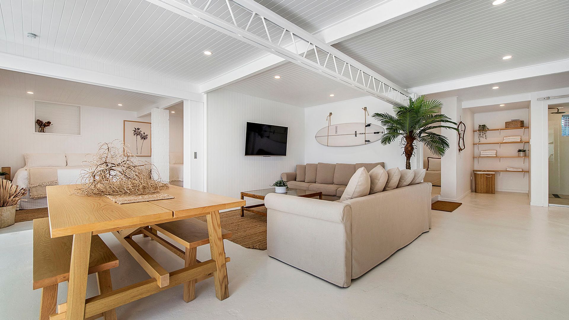 A spacious living area with a wooden dining table, a beige sofa, and a television mounted on the wall.