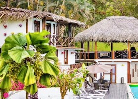 Um resort com área de piscina, estruturas com telhados de palha e vegetação exuberante.