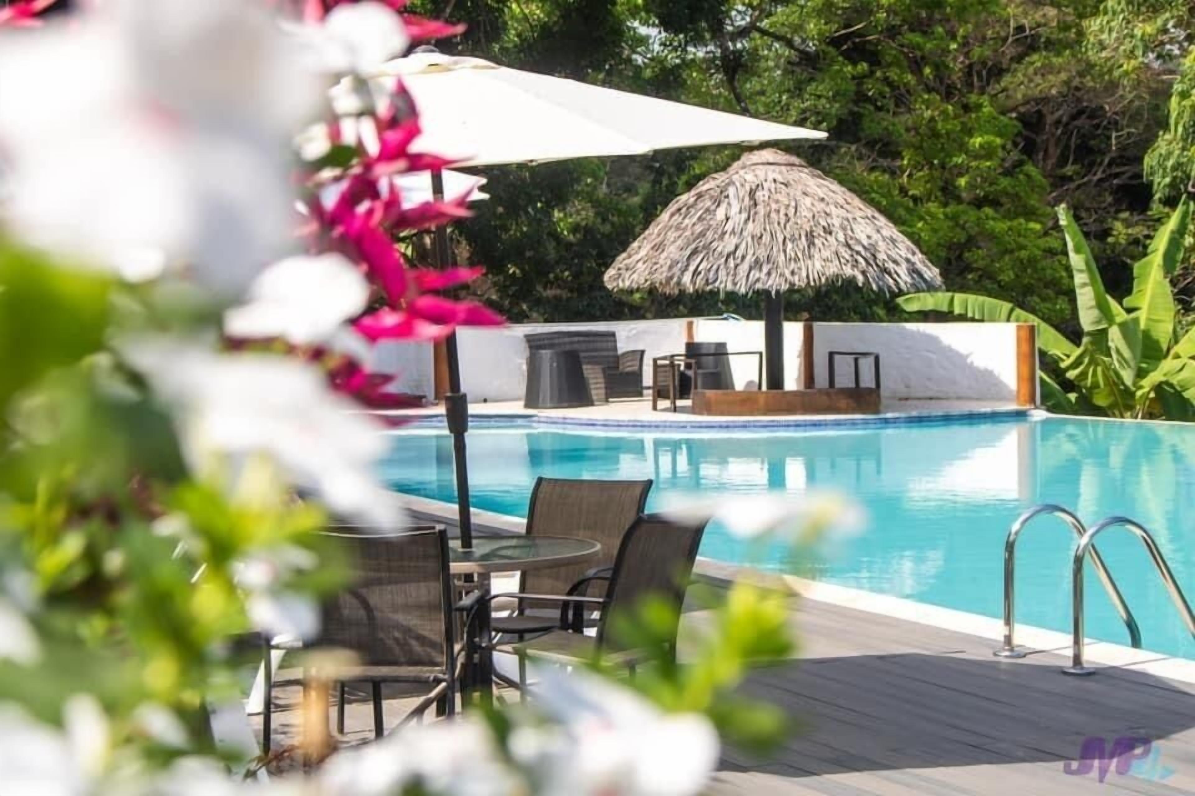 A pool area with a thatched umbrella, lounge chairs, and a table.