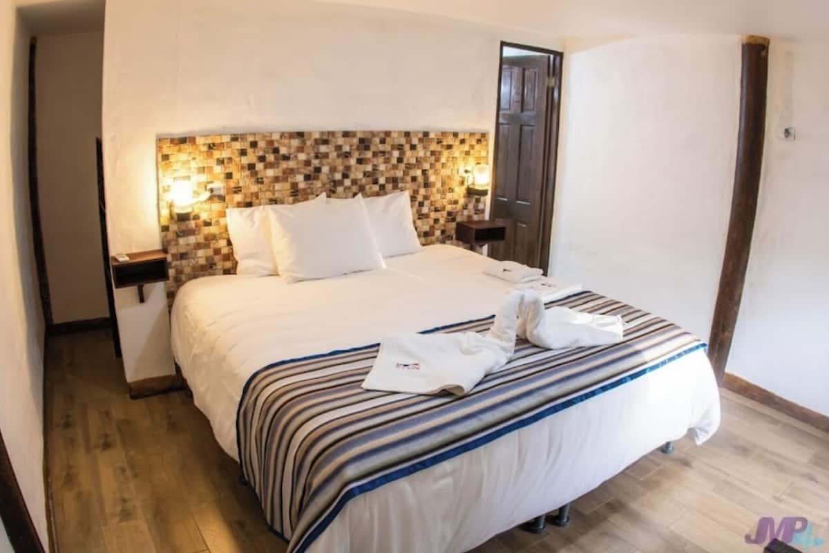 A neatly made bed with striped bedding, a checkered headboard, and a nightstand with a lamp.