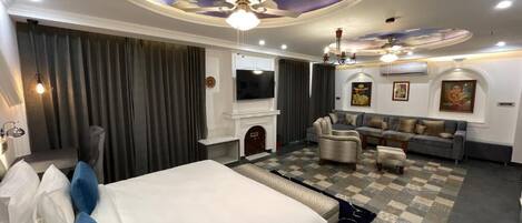 A hotel room with a large bed, a sofa, a TV, and a ceiling with a cloud design.