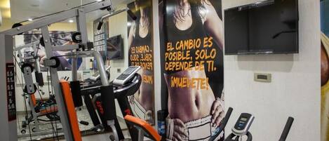 A gym with exercise equipment, a TV mounted on the wall, and motivational posters on the wall.