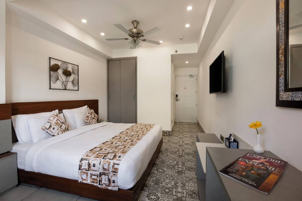 Una habitación de hotel con cama, escritorio, ventilador de techo, televisor y puerta que da al baño.