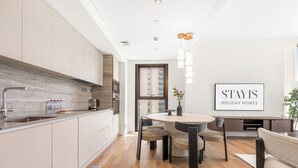 A modern kitchen with a marble backsplash, a dining area with a round table and chairs, and a framed sign on the wall. - Stayis- Luxurious 2 BR near Burj Khalifa (Dubai)