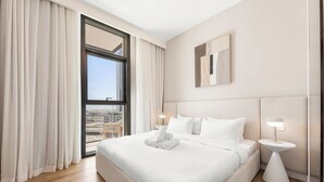 A hotel room with a large bed, two bedside tables with lamps, a view of the city through a large window, and a modern wall art piece. - Stayis- Luxurious 2 BR near Burj Khalifa (Dubai)