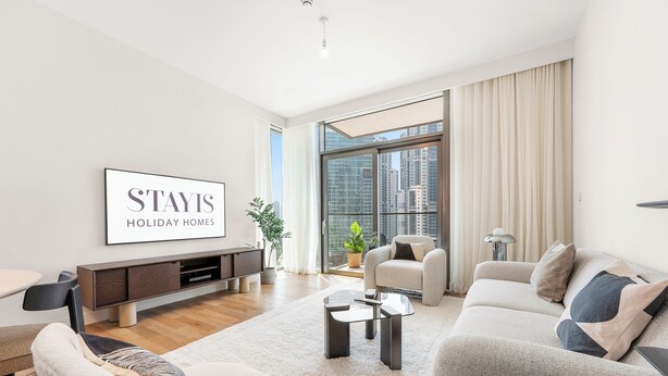 A modern living room with a sofa, armchairs, a coffee table, and a TV wall art. - Stayis- Luxurious 2 BR near Burj Khalifa (Dubai)
