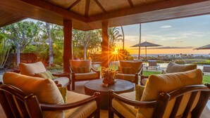 A covered outdoor seating area with chairs and a table, overlooking a scenic view of the ocean and sunset.