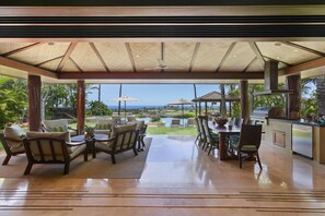 Um alpendre coberto ao ar livre com vista para o oceano, mobiliado com cadeiras, uma mesa e uma churrasqueira.
