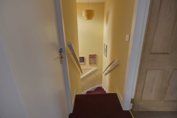 A narrow hallway with a wooden door on the right and a staircase leading to a landing with a light fixture. - Crossing Cottage Brora (Brora)