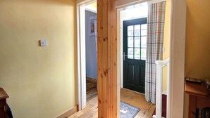 A hallway with wooden flooring, a door with a plaid curtain, and a doormat. - Crossing Cottage Brora (Brora)