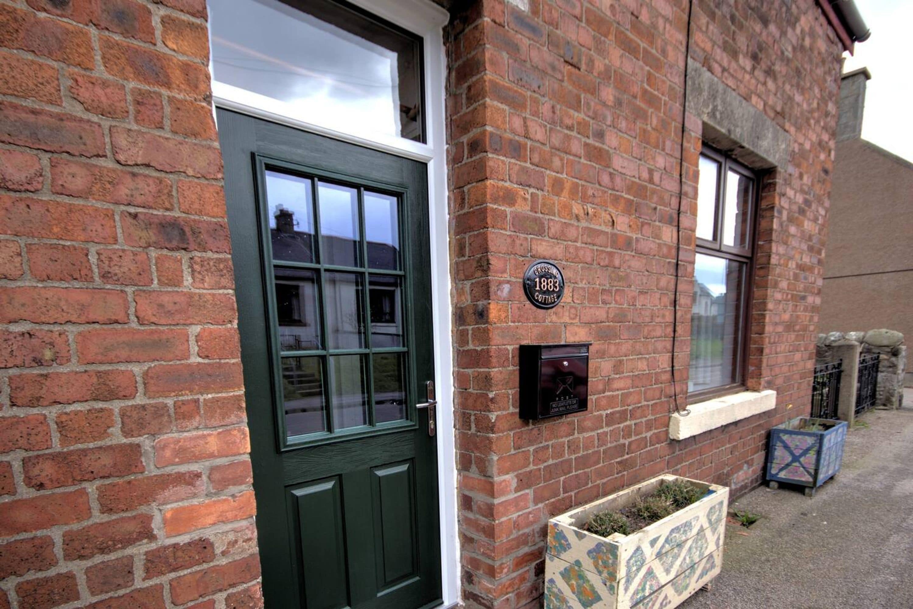 A brick building with a green door and windows. There is a plaque on the wall and a mailbox.