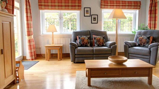 A living room with a sofa, armchair, wooden coffee table, and a lamp. - No 1 The Links Apartment Brora (Brora)