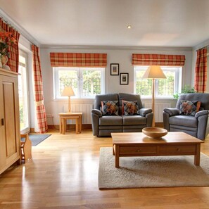 A living room with a sofa, armchair, wooden coffee table, and a lamp. - No 1 The Links Apartment Brora (Brora)