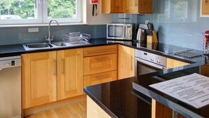 A modern kitchen with wooden cabinets, a stainless steel range hood, a microwave, and a dishwasher. - No 1 The Links Apartment Brora (Brora)