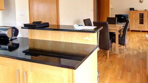 A modern kitchen with a black countertop, wooden cabinets, and a dining area with a table and chairs. - No 1 The Links Apartment Brora (Brora)