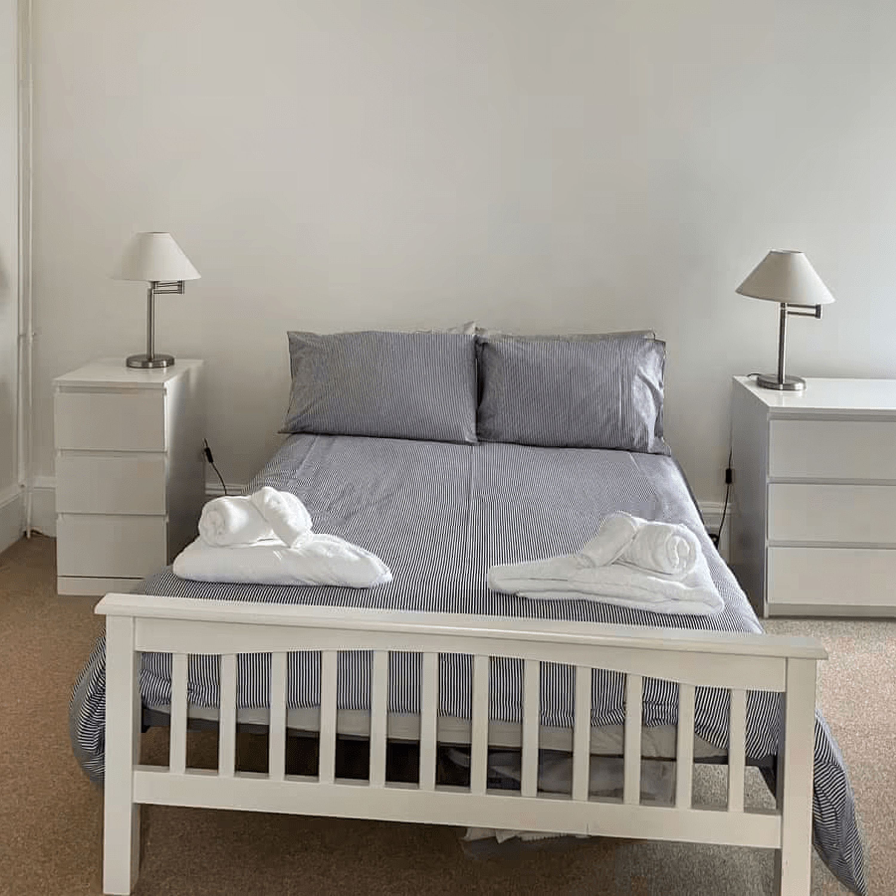 A neatly made bed with striped bedding, two bedside tables with lamps, and a white headboard.