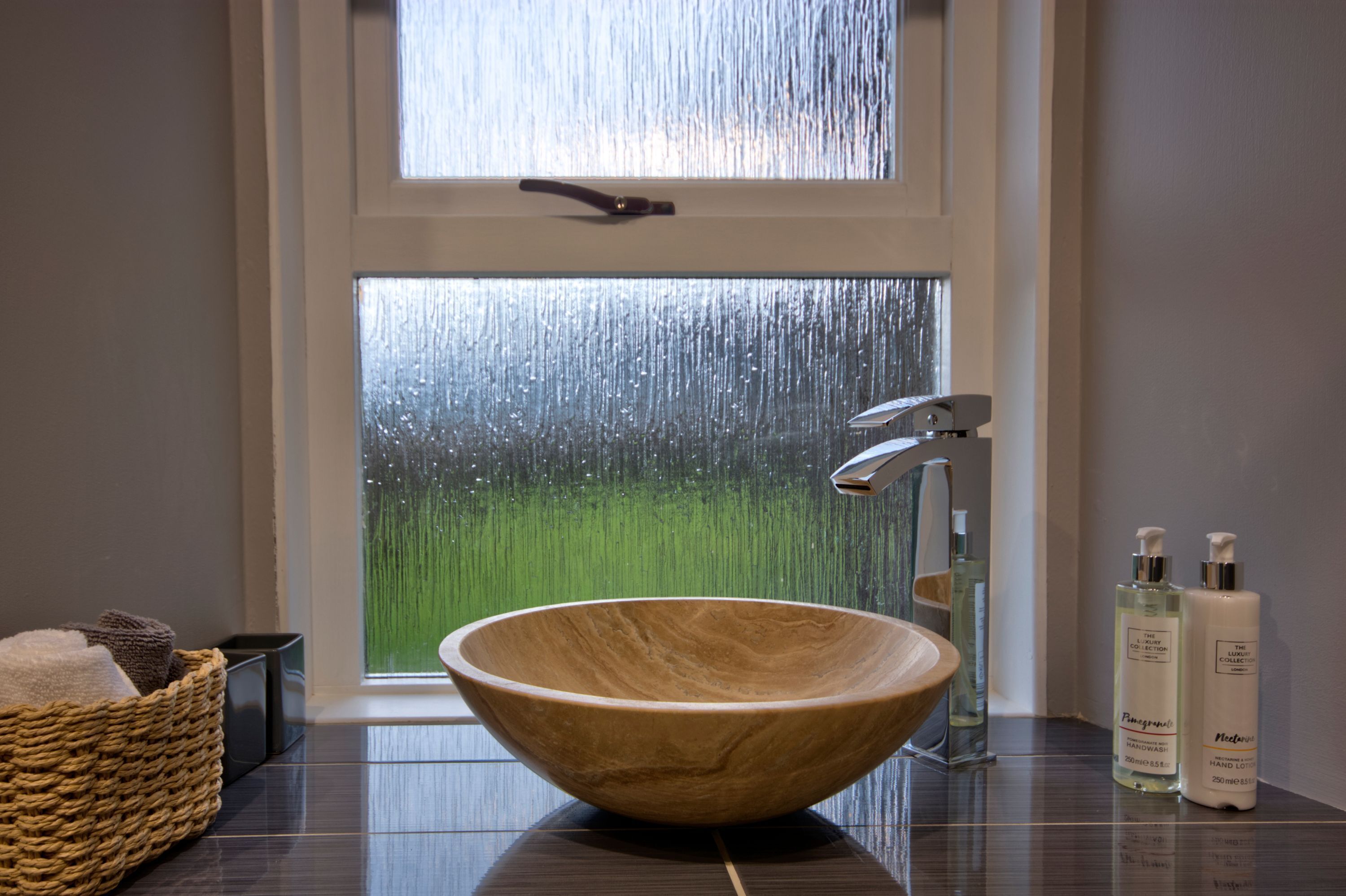 A wooden bowl sink in a bathroom with a view of a rainy garden through a window.