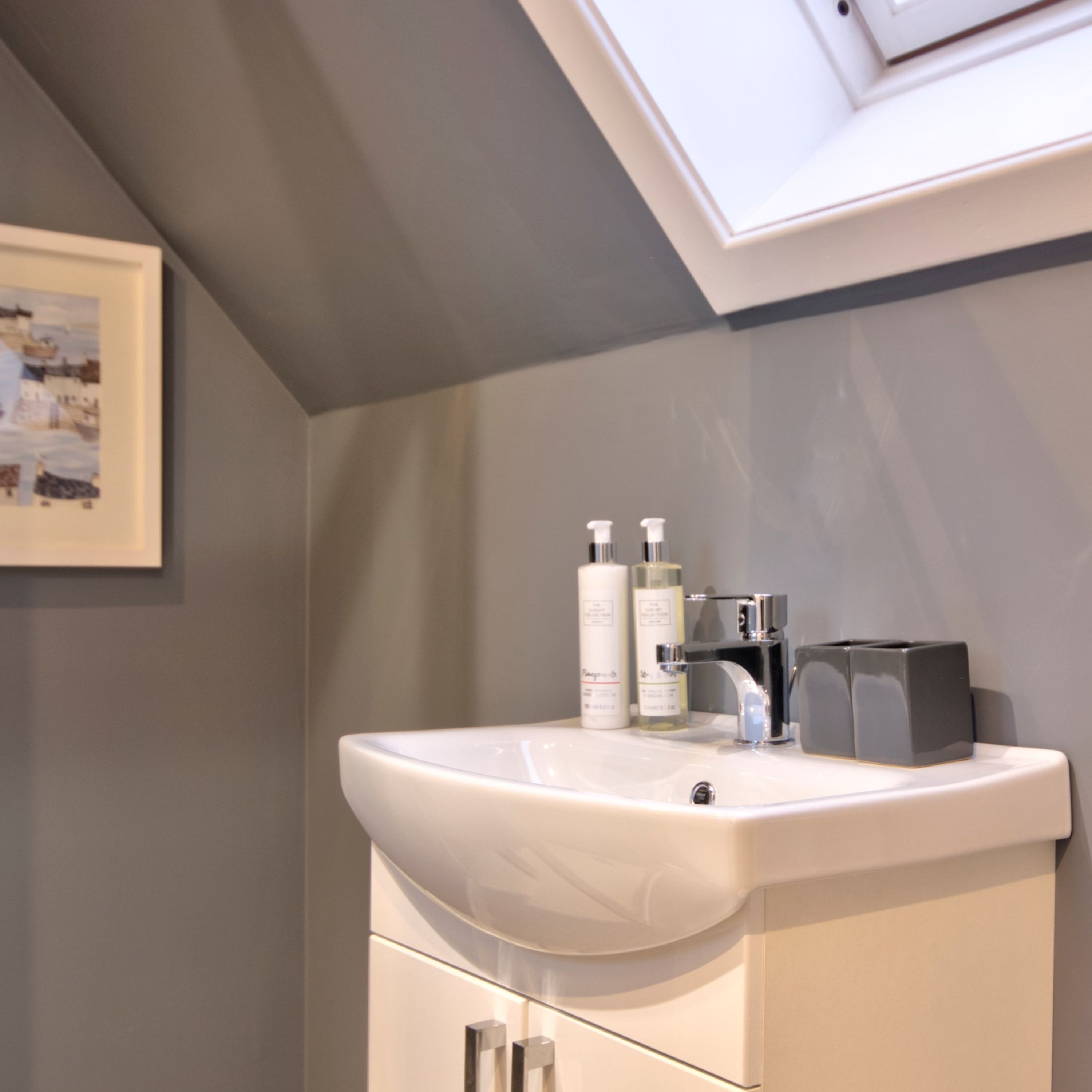 A bathroom with a white sink, two bottles of liquid soap, a soap dispenser, and a grey soap dispenser.