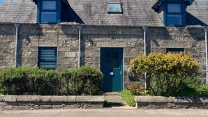 A stone house with a green door, two chimneys, and a small window. - Otago Cottage Brora (Brora)