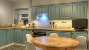 A kitchen with teal cabinets, a wooden dining table, and a built-in oven. - Otago Cottage Brora (Brora)