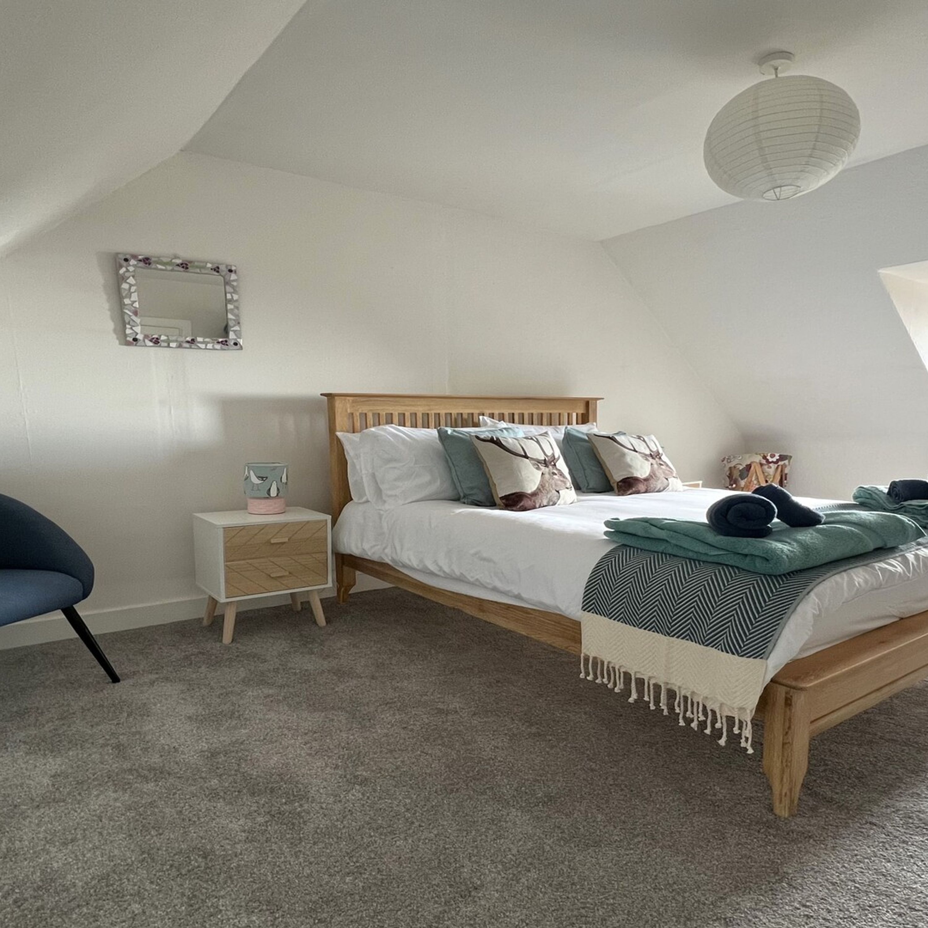 A bedroom with a wooden bed, a nightstand, a chair, a mirror, and a hanging light fixture.