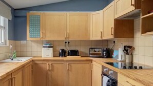 A compact kitchen with wooden cabinets, a built-in oven, and a countertop with a toaster and kettle. - Anvil House Golspie (Golspie)