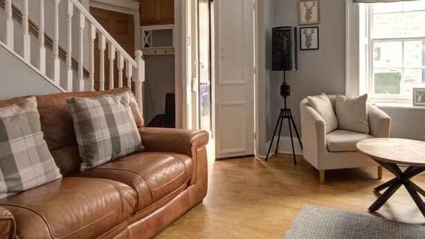 A living room with a brown leather sofa, a white armchair, and a round coffee table. - Anvil House Golspie (Golspie)