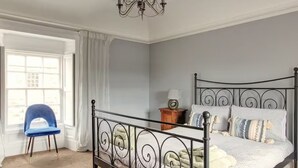 A bedroom with a four-poster bed, a chandelier, a chair, and a window with curtains. - Anvil House Golspie (Golspie)