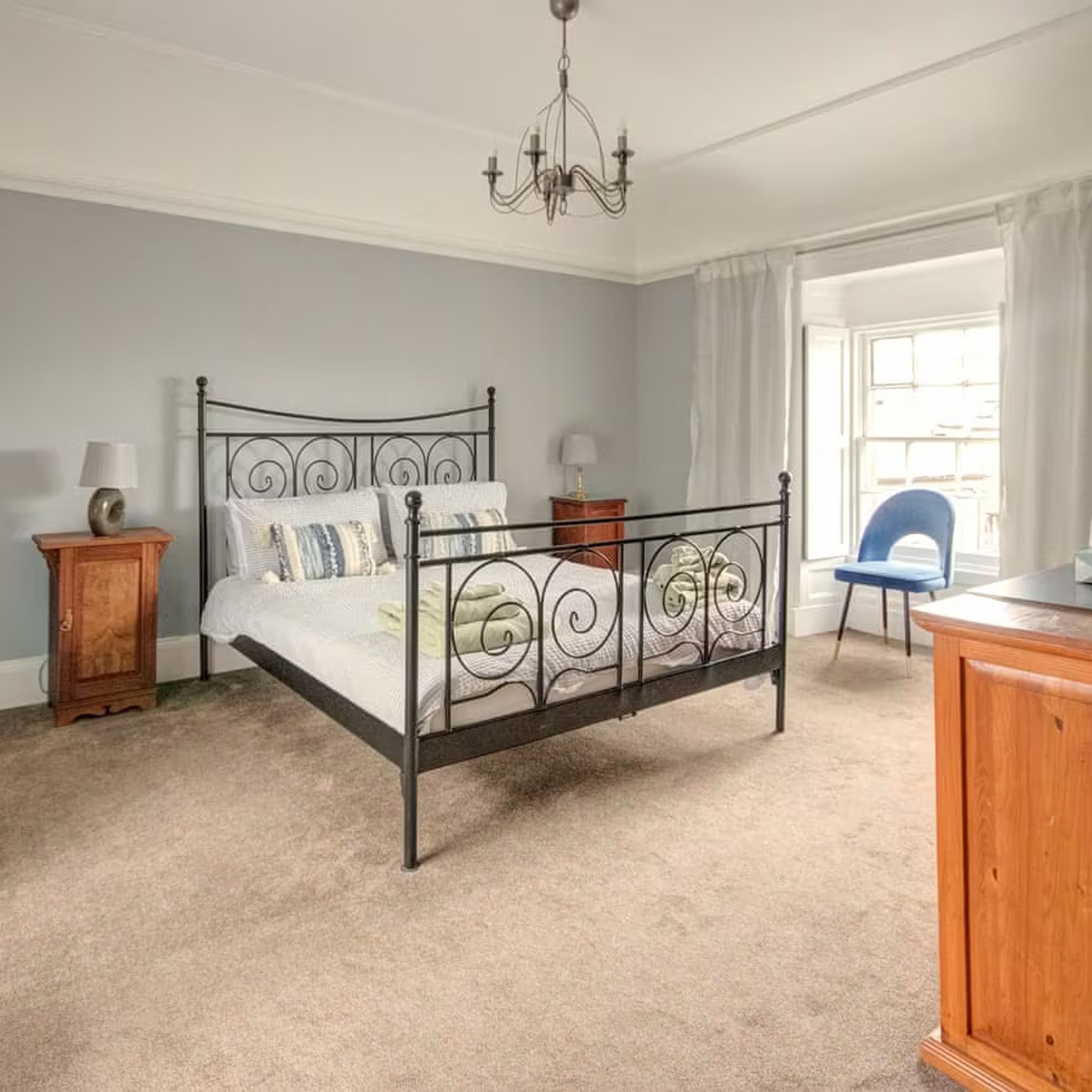 A bedroom with a metal bed frame, a wooden nightstand, a dresser, and a chair.