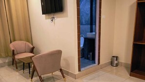 A modern living room with a flat-screen TV mounted on the wall, two armchairs, a sliding glass door leading to a balcony, and a small trash can. - Hotel Pinnacle Peaks (Joshimath)