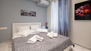 En snyggt bäddad säng med ett mönstrat överkast, en målning som föreställer en stadsbild och ett blommigt konstverk på väggen.