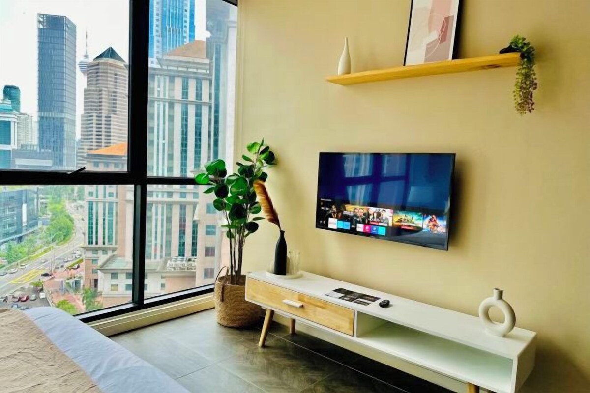 A modern living room with a large window, a flat-screen TV, a white console table, and a potted plant.
