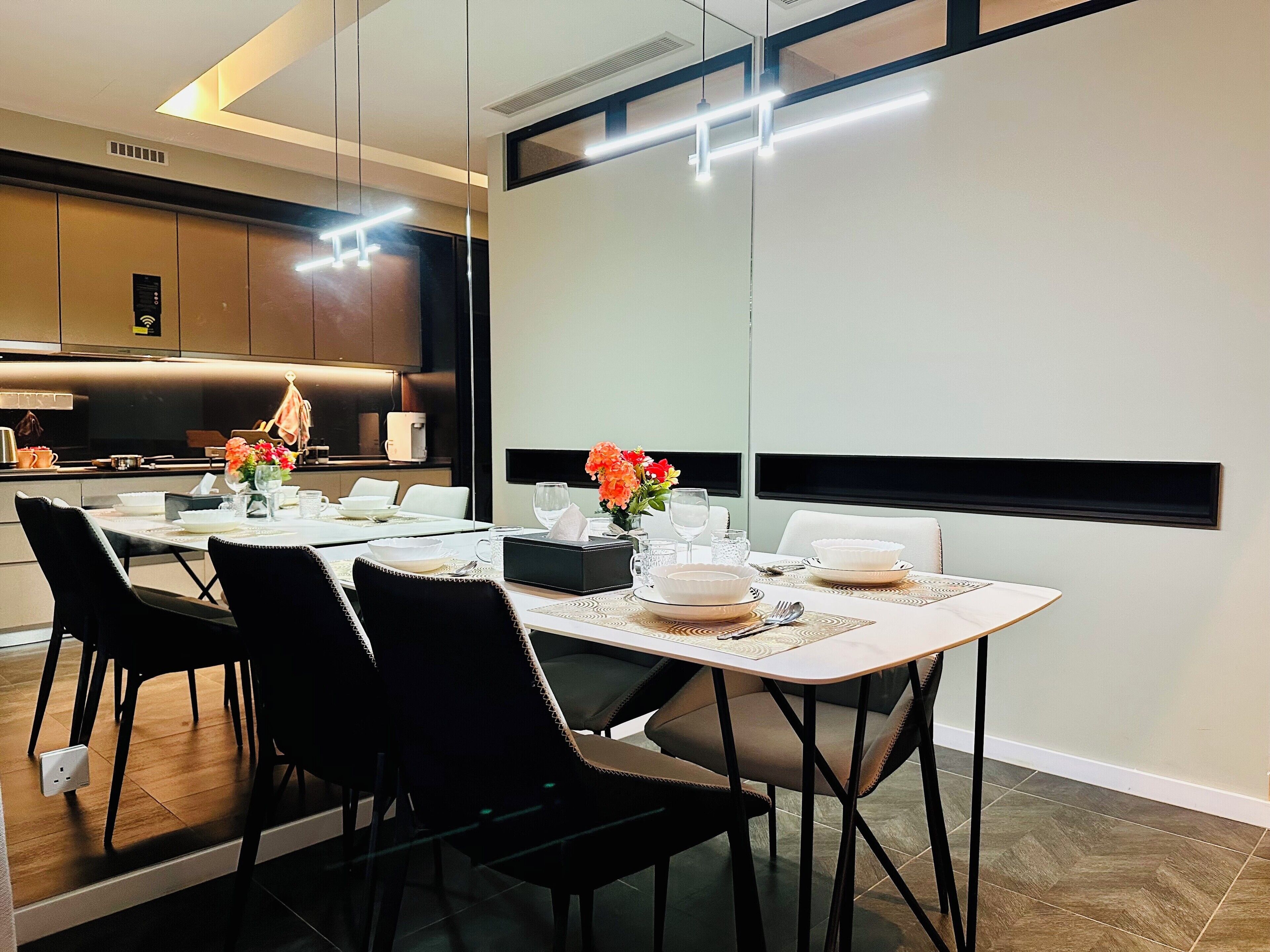 A modern dining area with a white table set for four, black chairs, and a kitchen in the background.