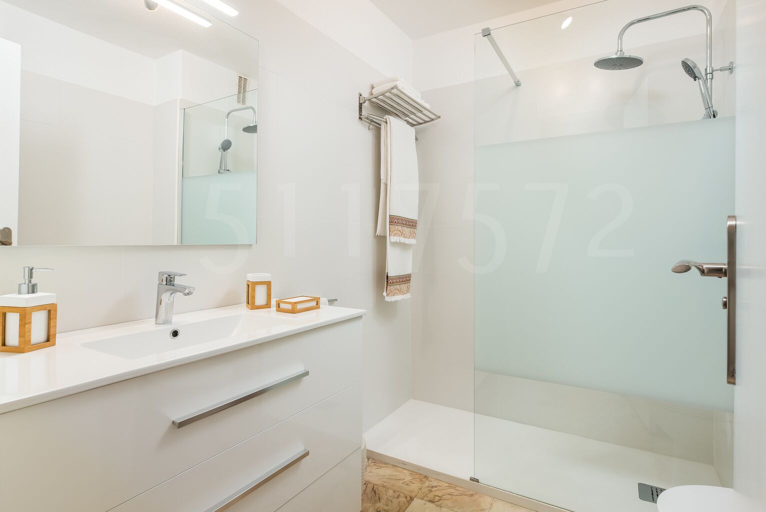 Ein modernes Badezimmer mit Duschkabine aus Glas, einem großen Spiegel und einem weißen Waschtisch mit Spüle und Handtuchhalter.